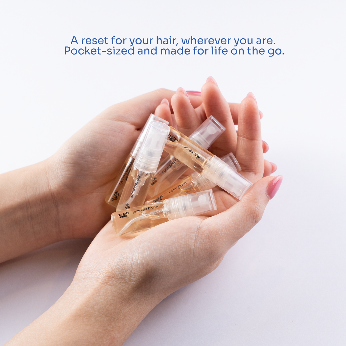 A pair of hands holding several small clear spray vials filled with hair perfume liquid, with blue text above reading 'A reset for your hair, wherever you are. Pocket-sized and made for life on the go.