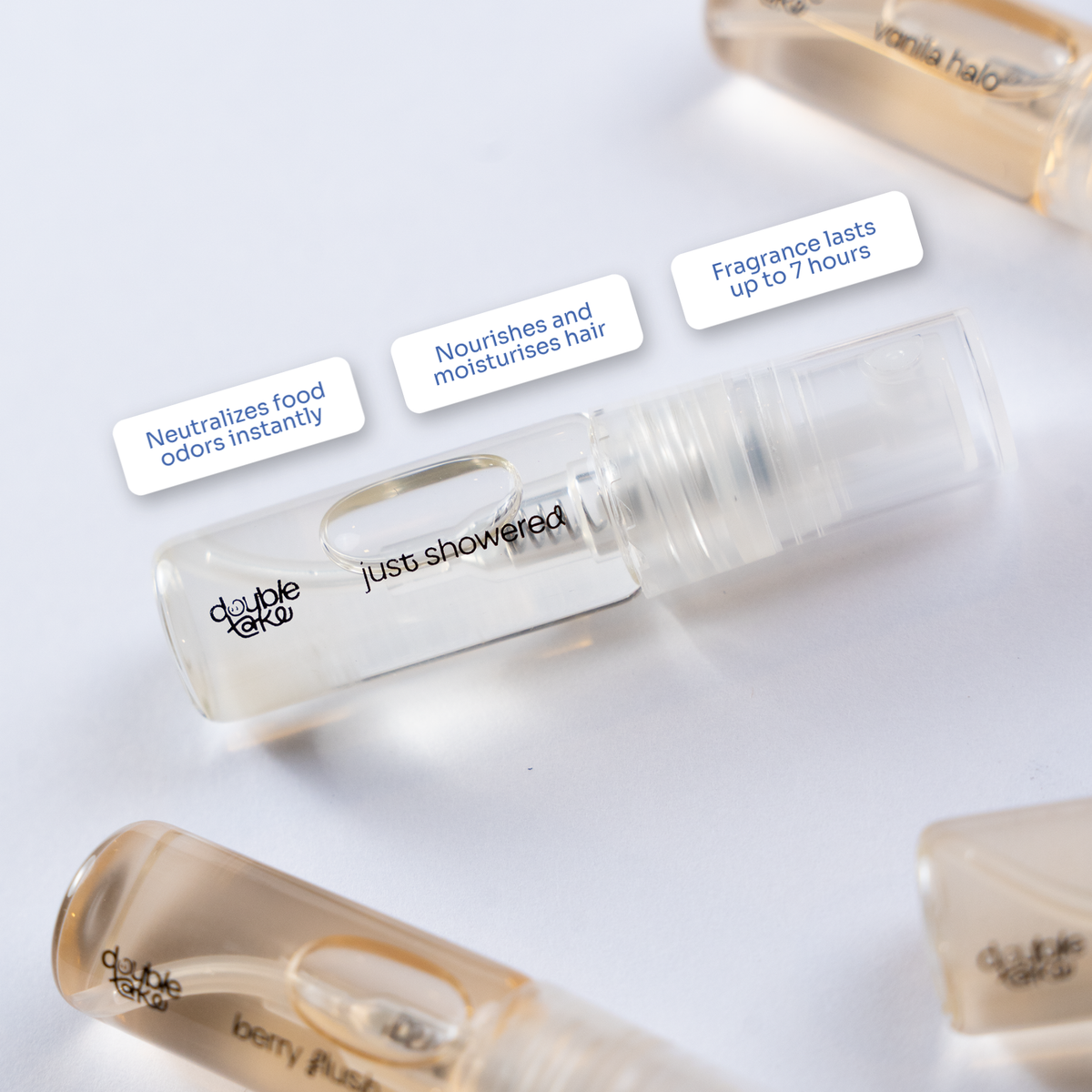 A clear cylindrical travel-sized spray bottle labeled 'just showered' by double color, shown on a white background with three white text callouts and partial other bottles around it.
